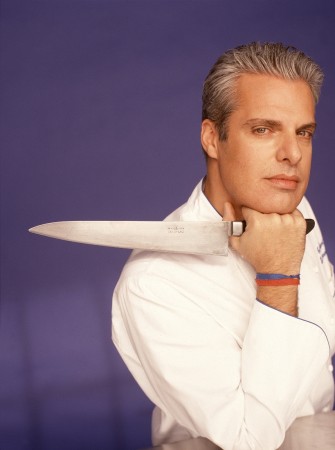 Eric Ripert, chef, resting his chin on his right hand, which is holding a large kitchen knife pointed over his right shoulder.