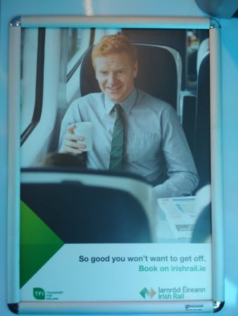 Irish Rail poster of a man on a train holding a cup with one hand, the other cannot be seen and may be at waist level. The marketing slogan across the bottom reads, "So good you won't want to get off."